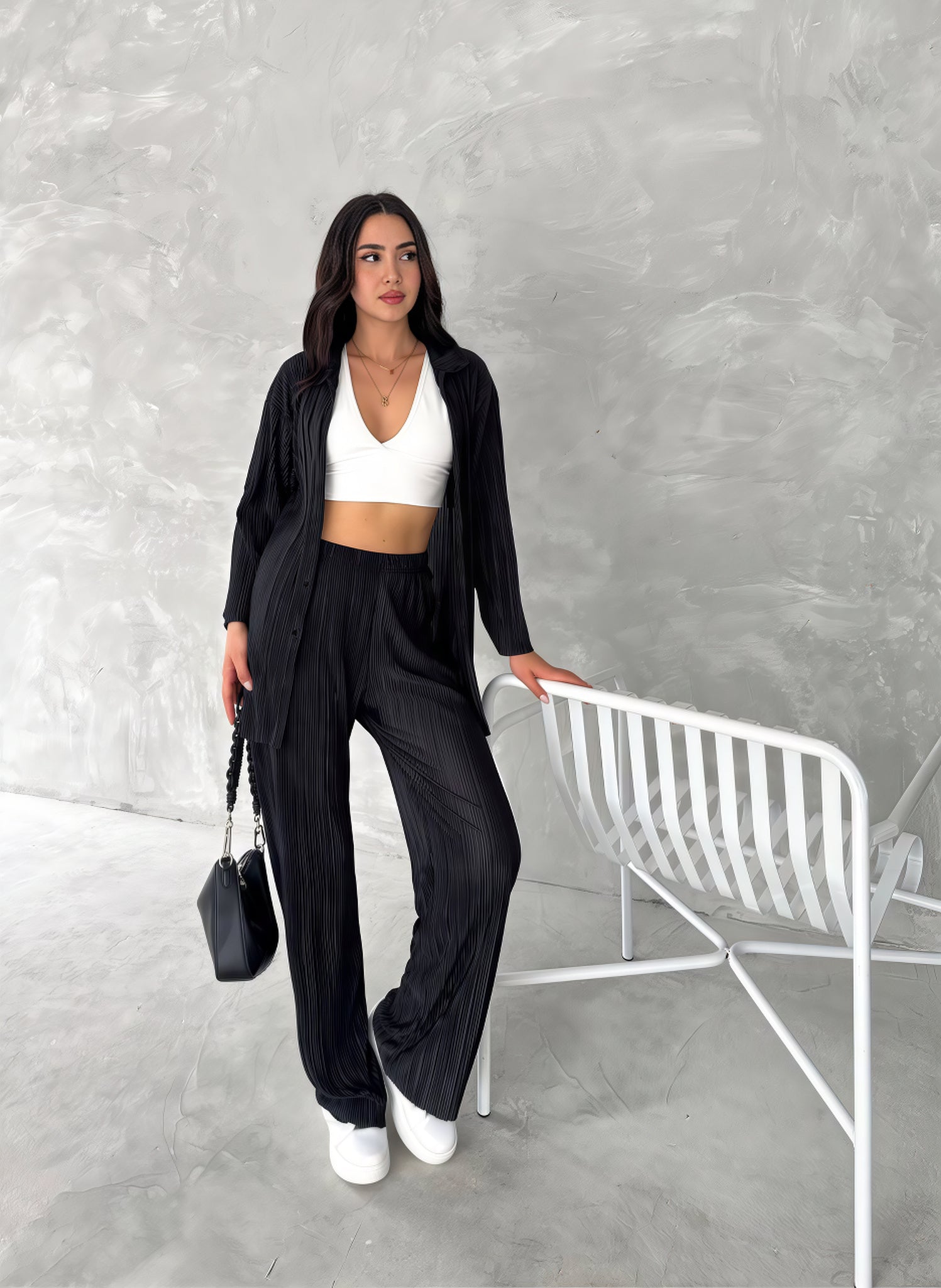 Woman in black outfit with white top against a gray wall